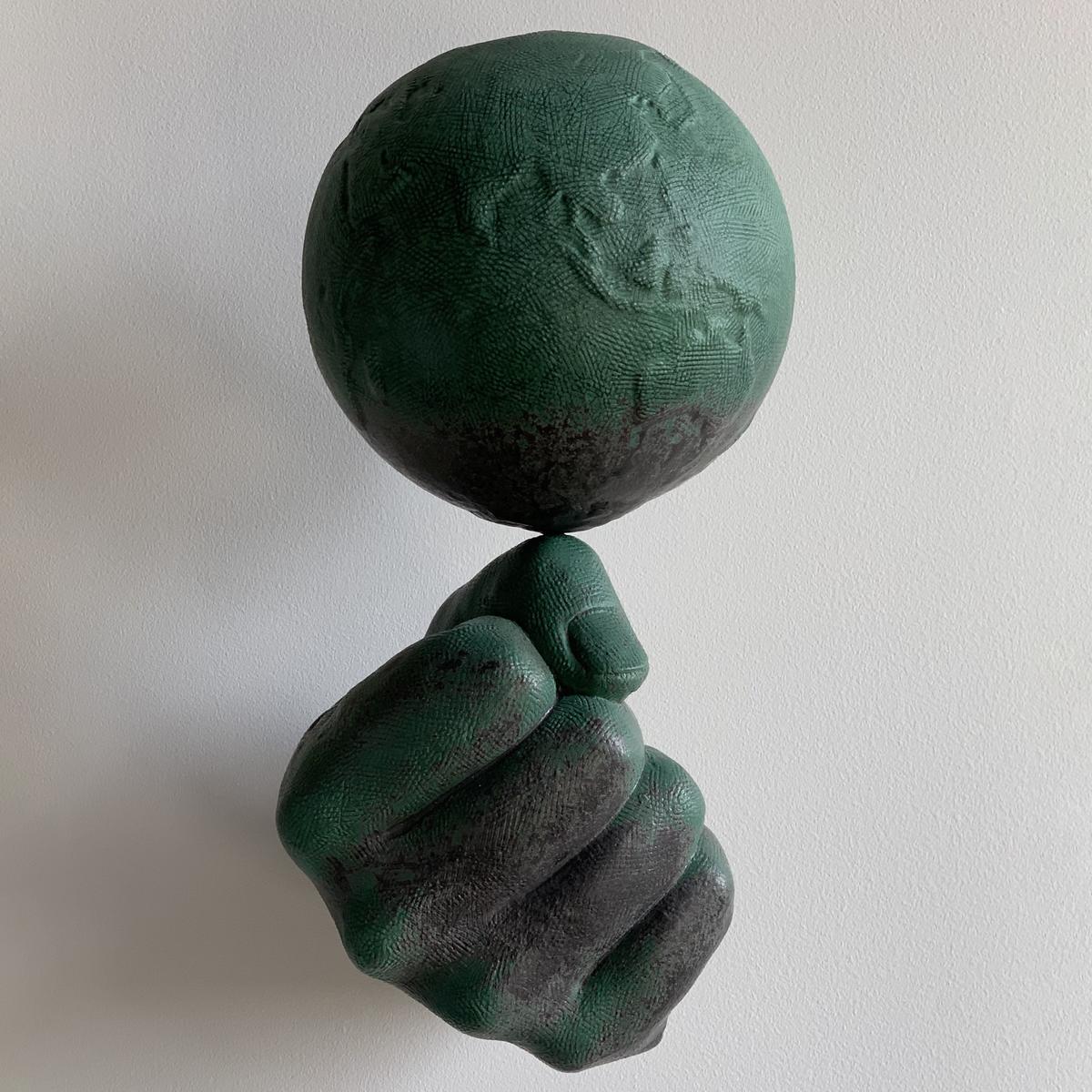 Ceramic wall sculpture of a fist balancing the earth.